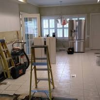Kitchen under renovation with ladder, tools, and stainless steel refrigerator in tiled room