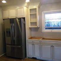 Modern kitchen with stainless steel fridge, white cabinets, wood countertops, and a window