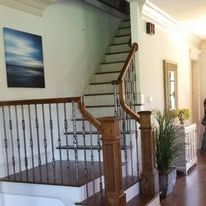 Staircase with wooden banister in a bright hallway, with wall art and a potted plant.
