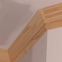 Wooden stair handrail corner joint against a white wall and ceiling.
