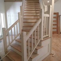 White staircase with wooden steps and white railings in a hallway, viewed from the bottom.