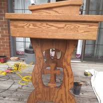 Wooden podium with carved decorative base on a deck, with tools and extension cords nearby.