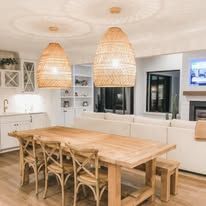 Bright modern kitchen with a wooden dining table, woven pendant lights, and white cabinets