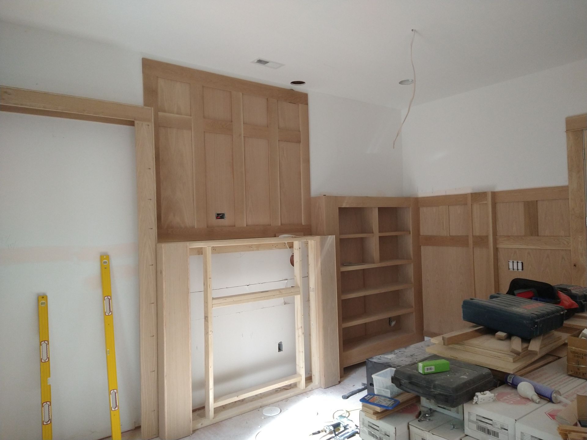 Wooden kitchen cabinets being installed in a room with tools and materials scattered on the floor.