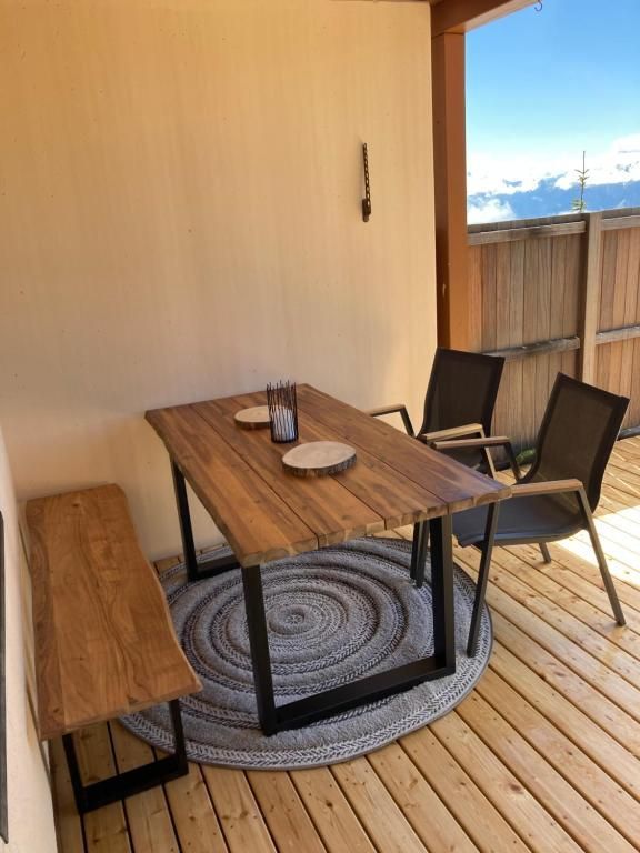 Essgruppe für den Außenbereich auf der Terrasse mit Holztisch, schwarzen Stühlen und Bank auf einem gestreiften Teppich.