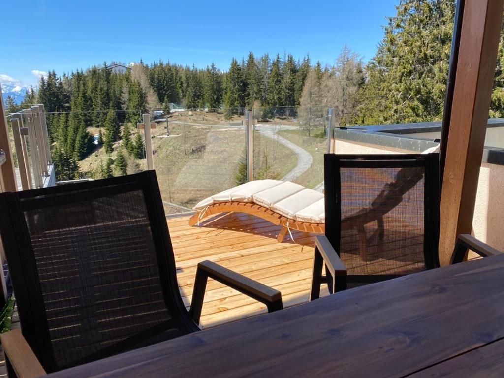 Holzliegen mit Blick auf einen schneebedeckten Berghang und einen Kiefernwald unter klarem, blauem Himmel