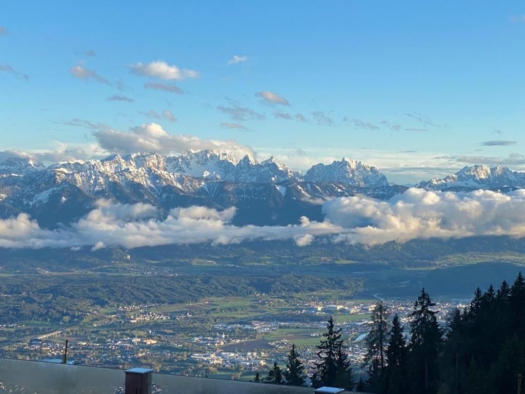 Schneebedeckte Bergkette über einer Talstadt unter blauem Himmel, gesehen von einem bewaldeten Hügel