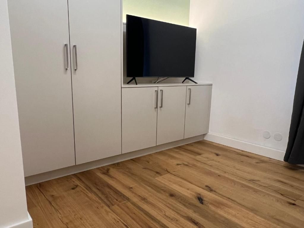Minimalistisches Wohnzimmer mit weißen Schränken, einem Fernseher auf einem Ständer und Holzboden.