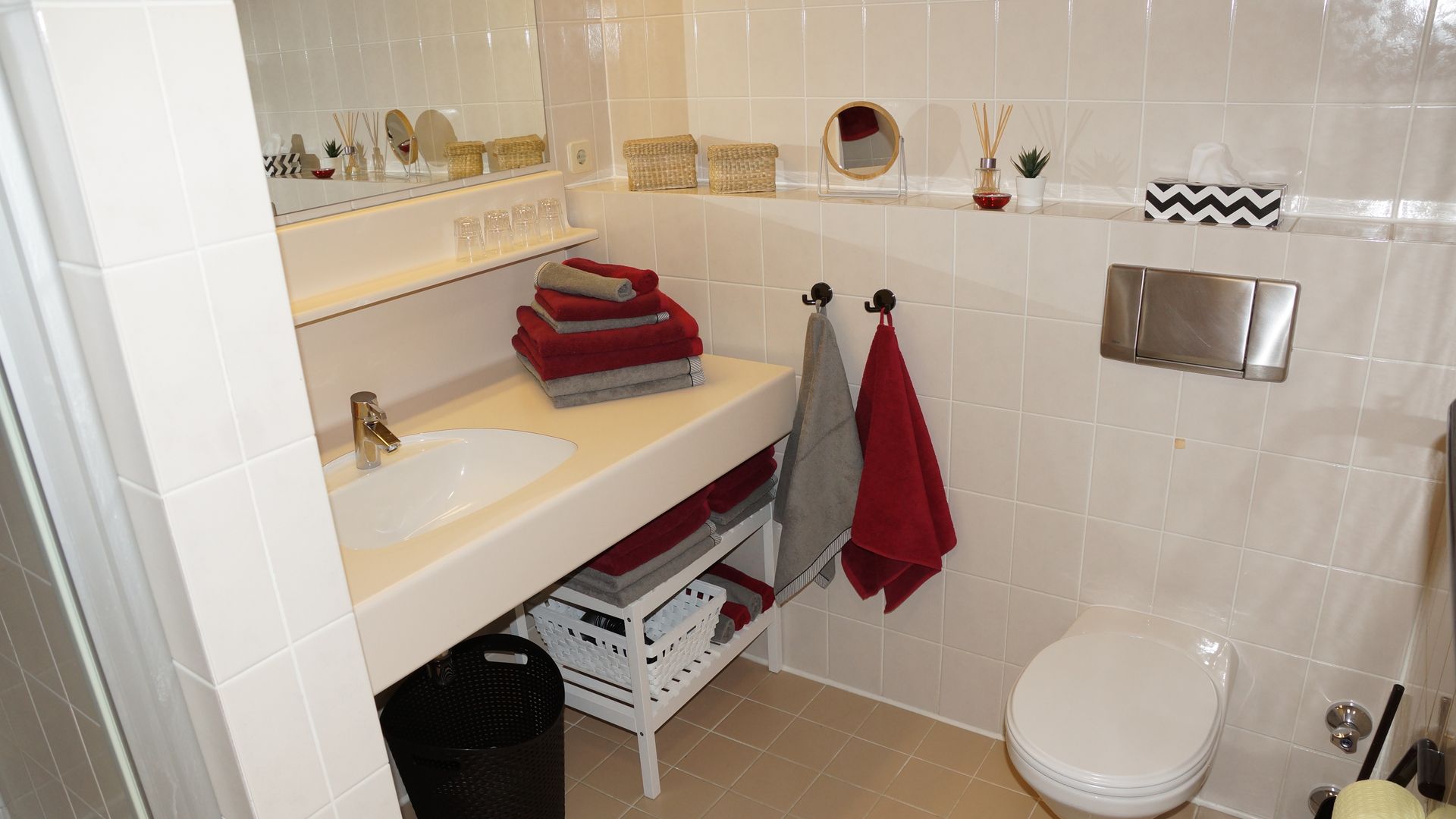 Barrierefreies Badezimmer mit weißem Waschbecken, beigefarbenen Fliesen, roten Handtüchern und Toilette