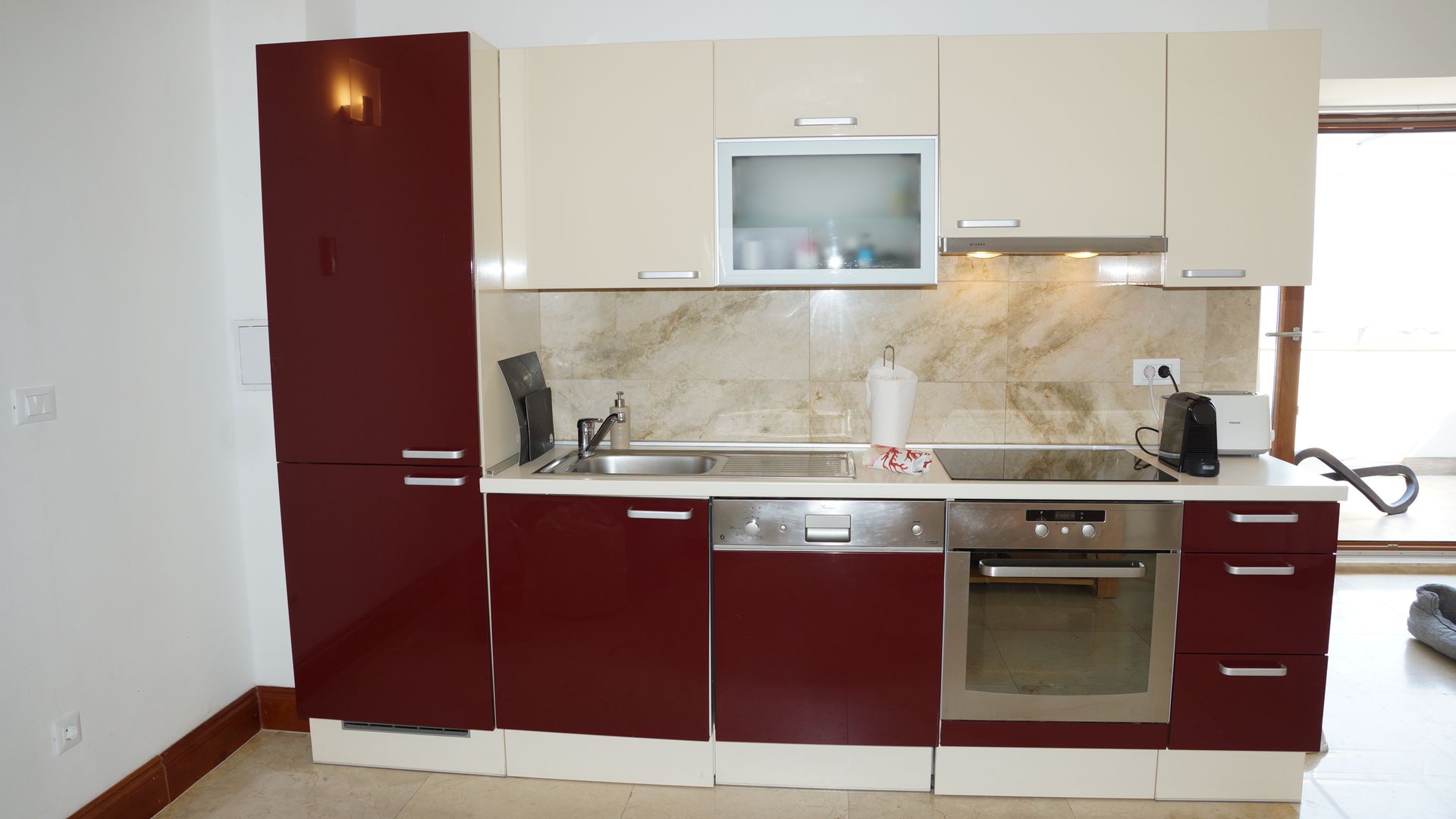 Moderne Küche mit bordeauxroten und cremefarbenen Schränken, Edelstahlgeräten und Marmor-Spritzschutz