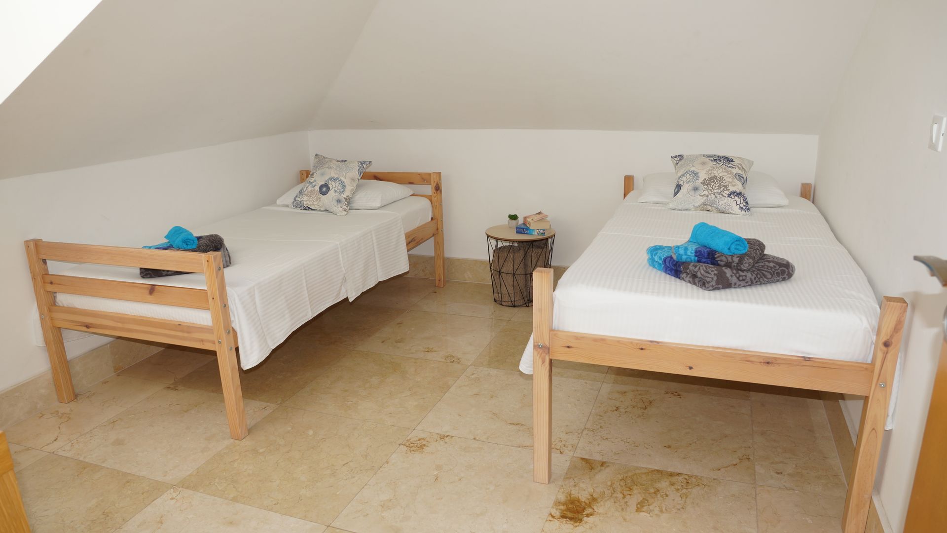Kleines Dachgeschosszimmer mit zwei hölzernen Einzelbetten, weißer Bettwäsche und gefalteten blauen Handtüchern darauf.