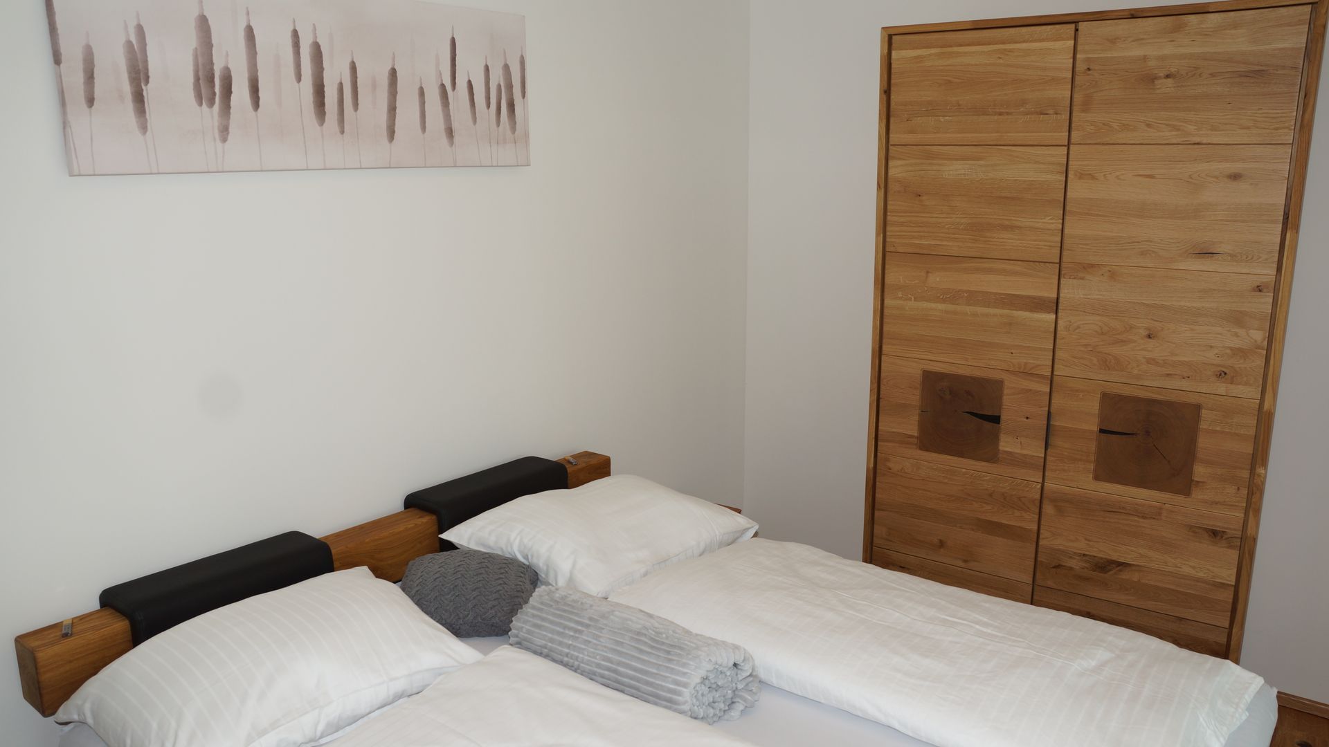 Minimalistisches Schlafzimmer mit zwei Einzelbetten, weißer Bettwäsche und einem Holzschrank.