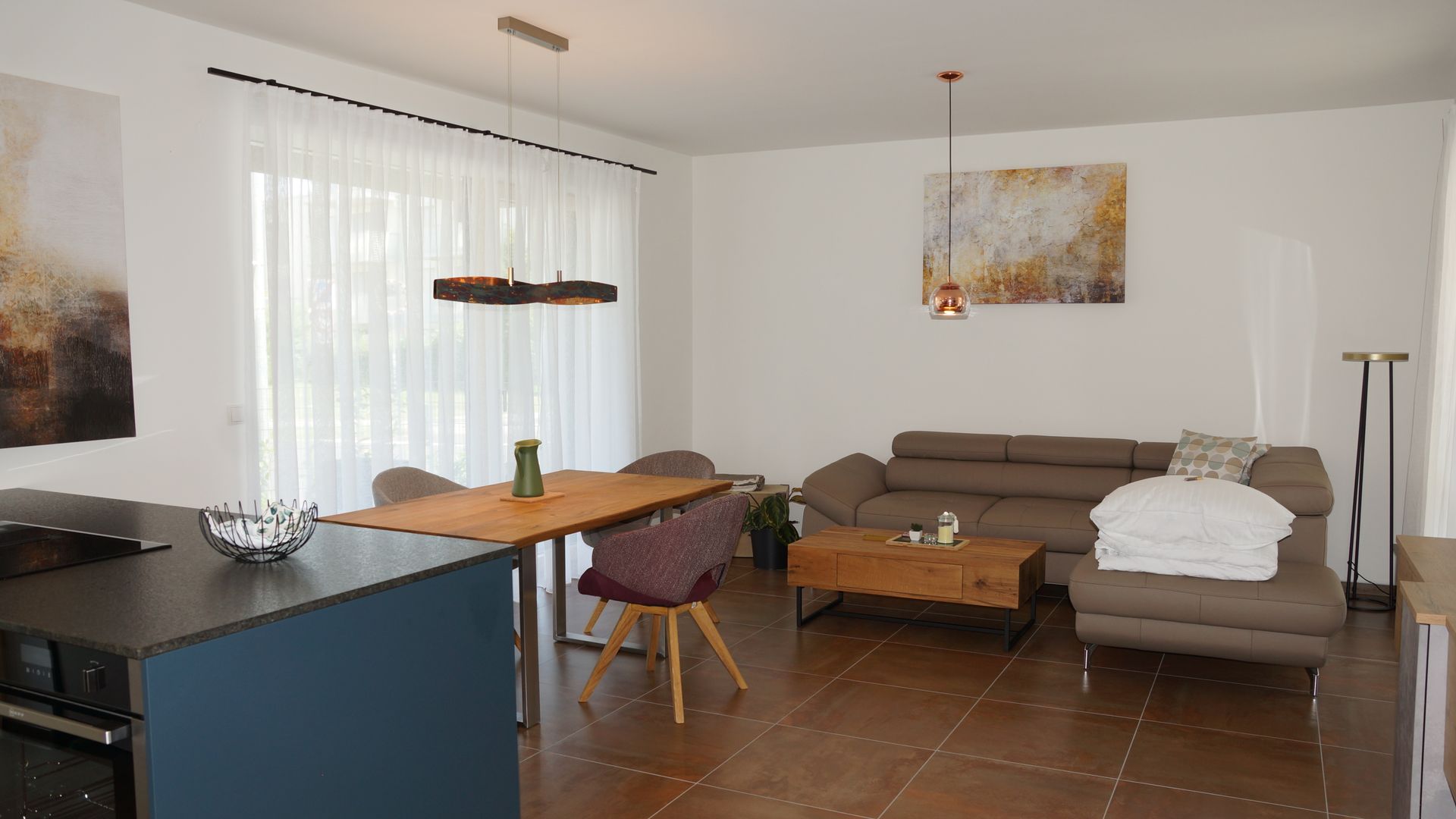 Helles Wohnzimmer mit Ecksofa, Couchtisch, Esstisch und Stehlampe auf Fliesenboden.