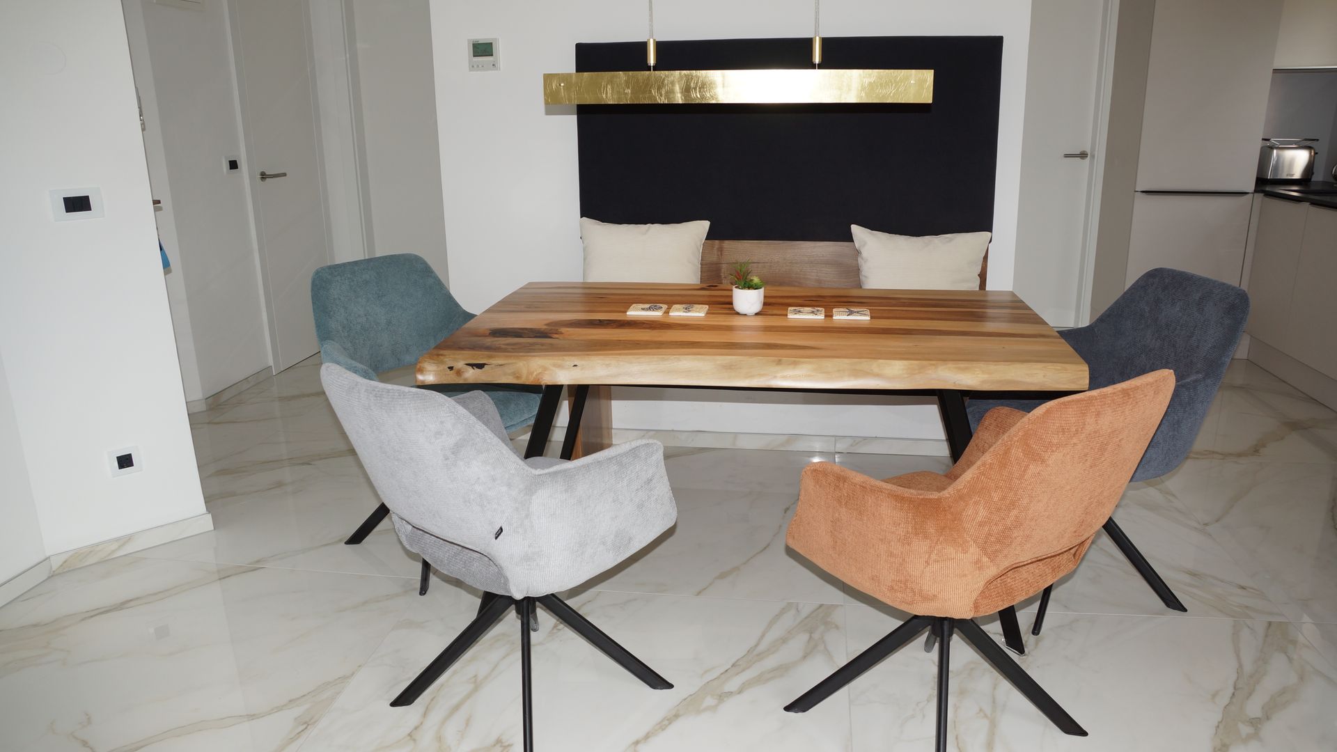 Modernes Esszimmer mit Holztisch, vier Drehstühlen und einer schwarzen Pendelleuchte über Marmorboden.