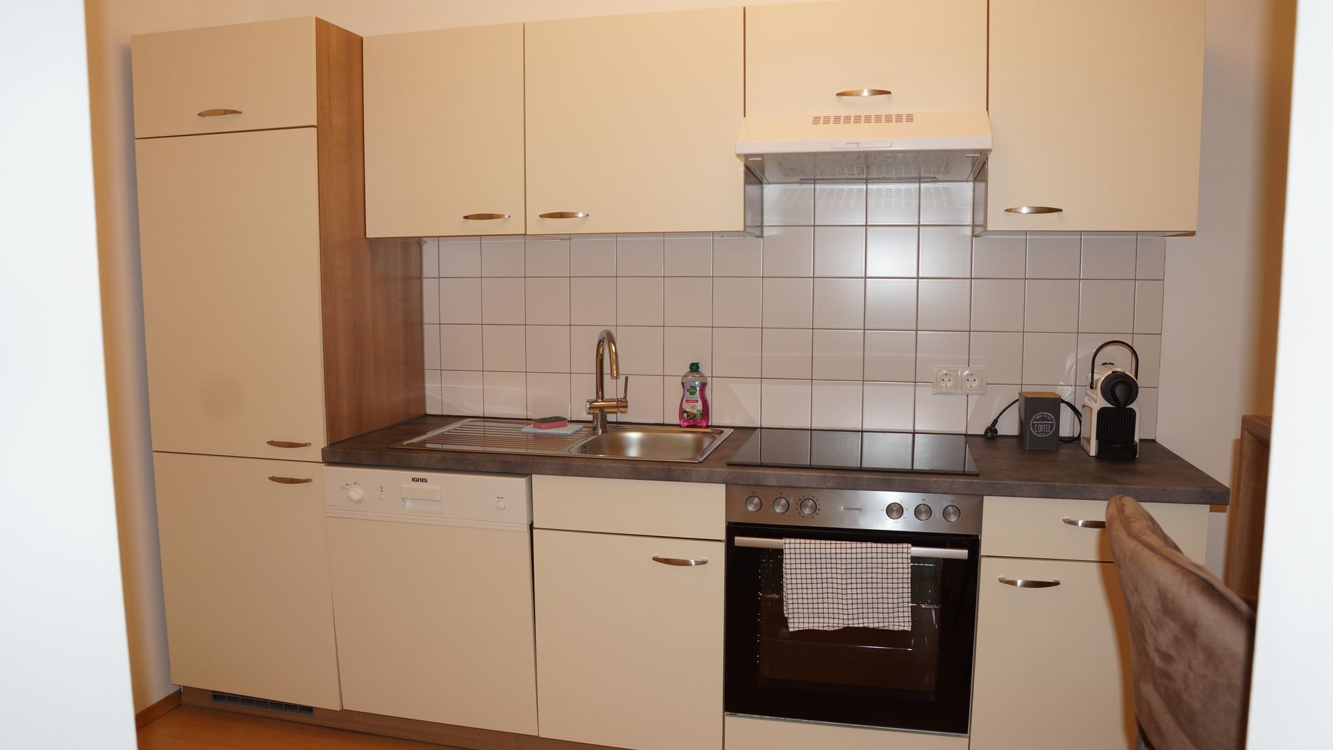 Moderne Küche mit beigen Schränken, schwarzer Arbeitsplatte, gefliestem Spritzschutz, Backofen, Spüle