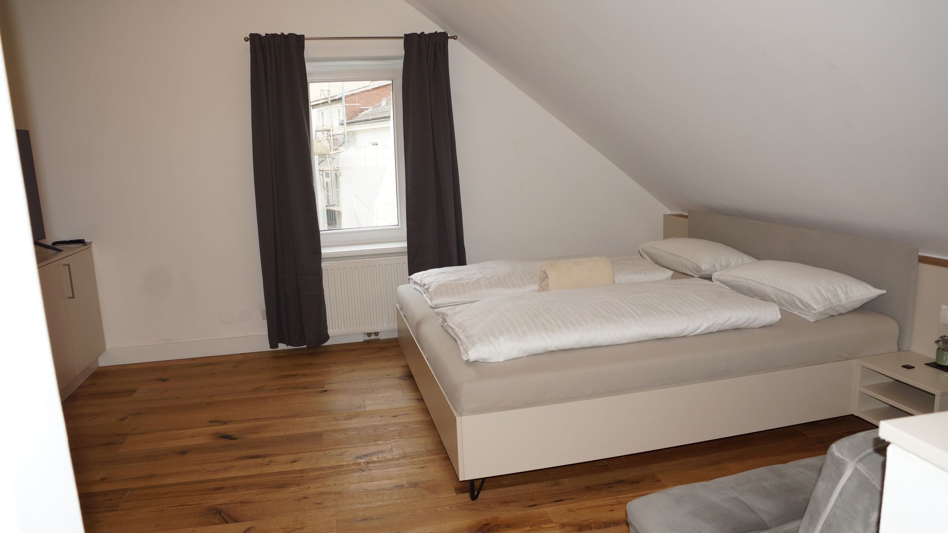 Minimalistisches Dachgeschoss-Schlafzimmer mit weißem Bett, dunklen Vorhängen und Holzboden