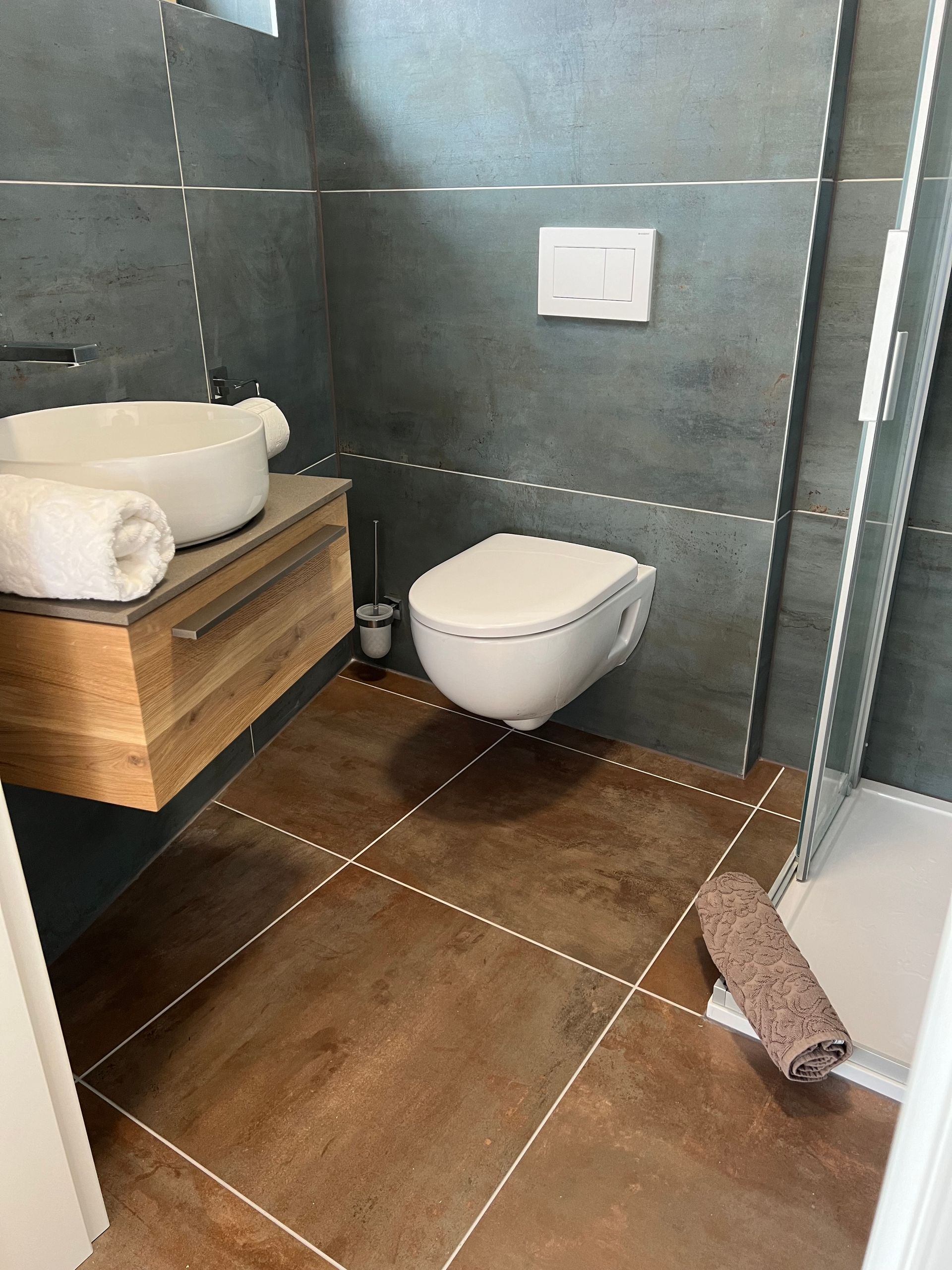Modernes Badezimmer mit wandhängendem Waschbecken, wandhängender Toilette, grauen Fliesen und braunem Boden;