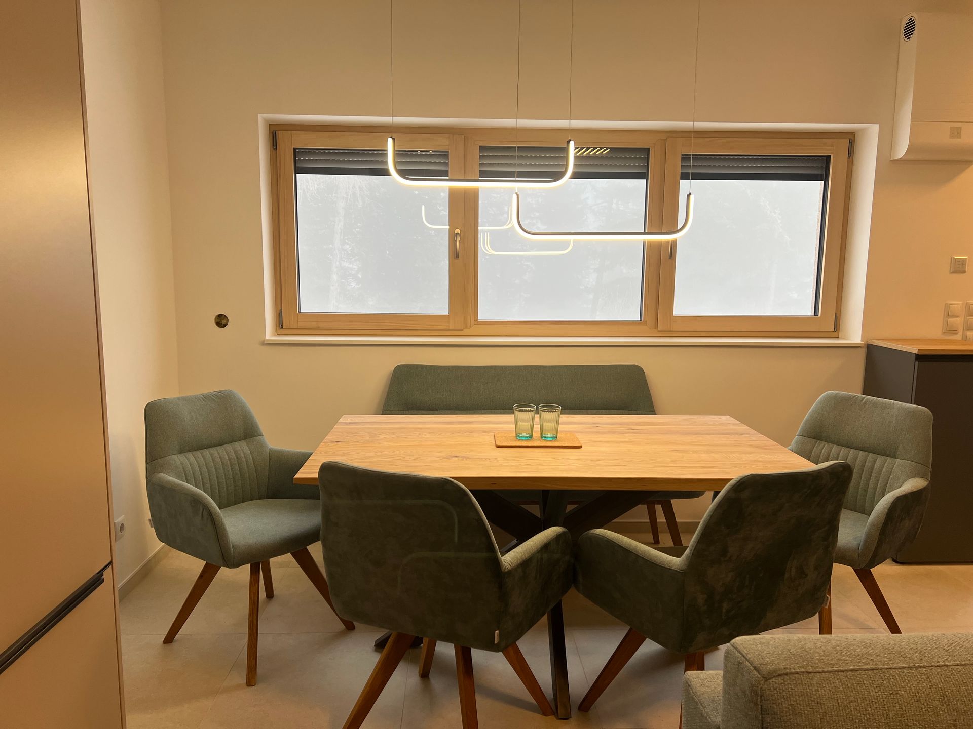 Moderner Besprechungsraum mit Holztisch, grünen Stühlen und einem großen Fenster über dem Tisch
