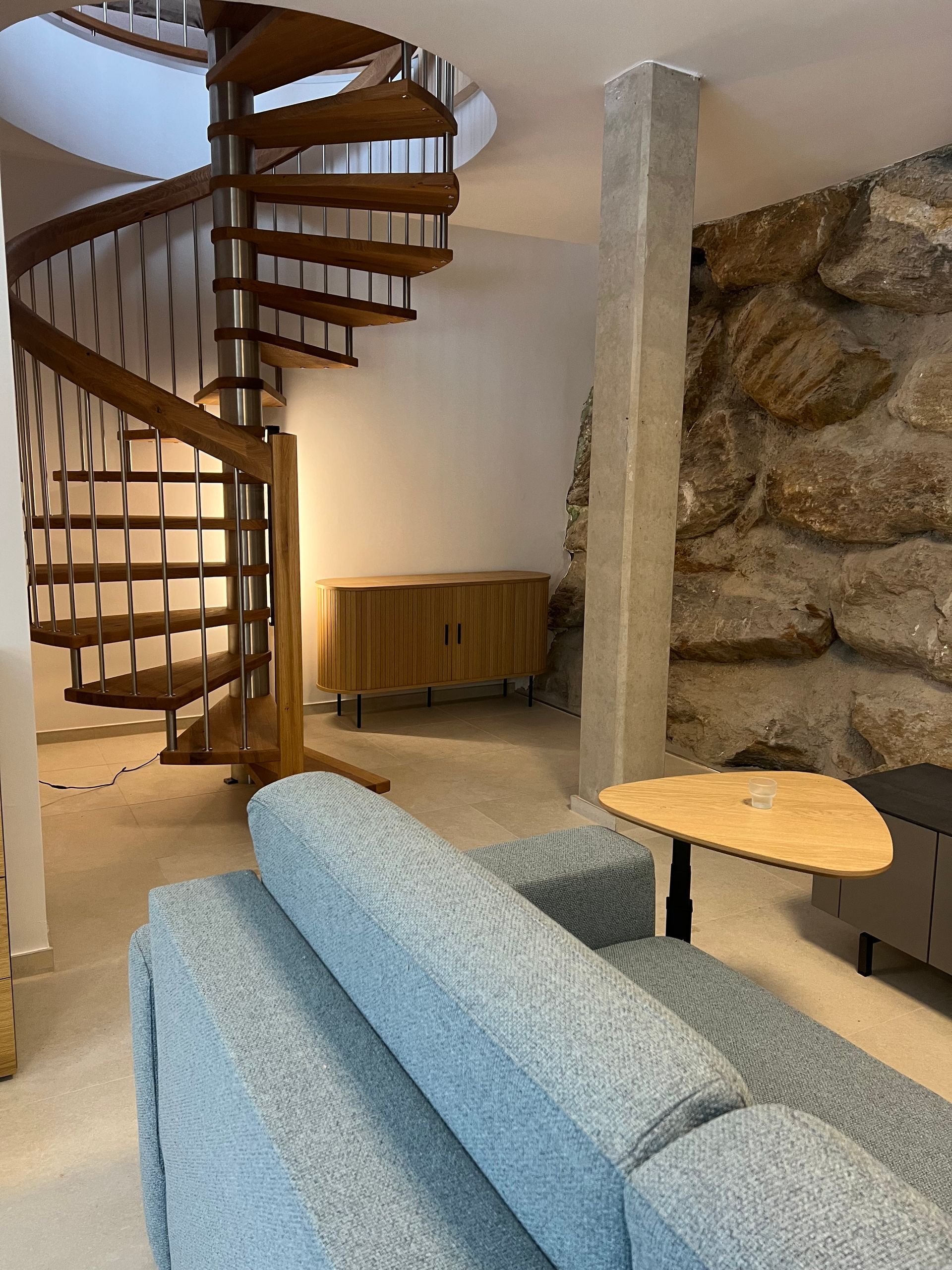 Wohnzimmer mit Wendeltreppe, blauem Sofa, Holztisch und Steinwanddetail