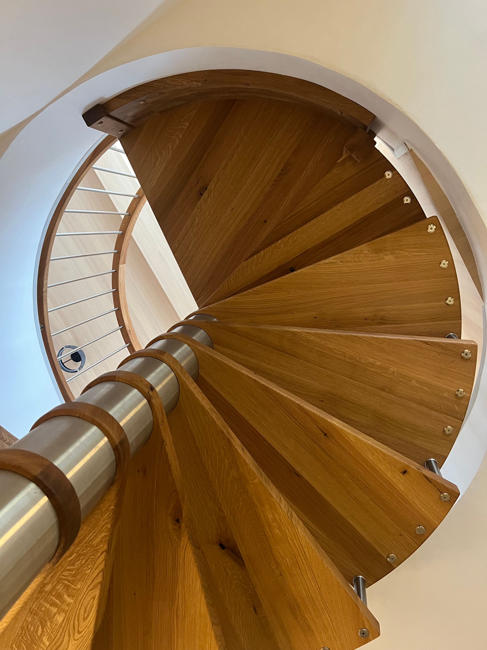 Von unten gesehen eine spiralförmige Holztreppe mit weißen Wänden und einem zentralen Metallhandlauf.