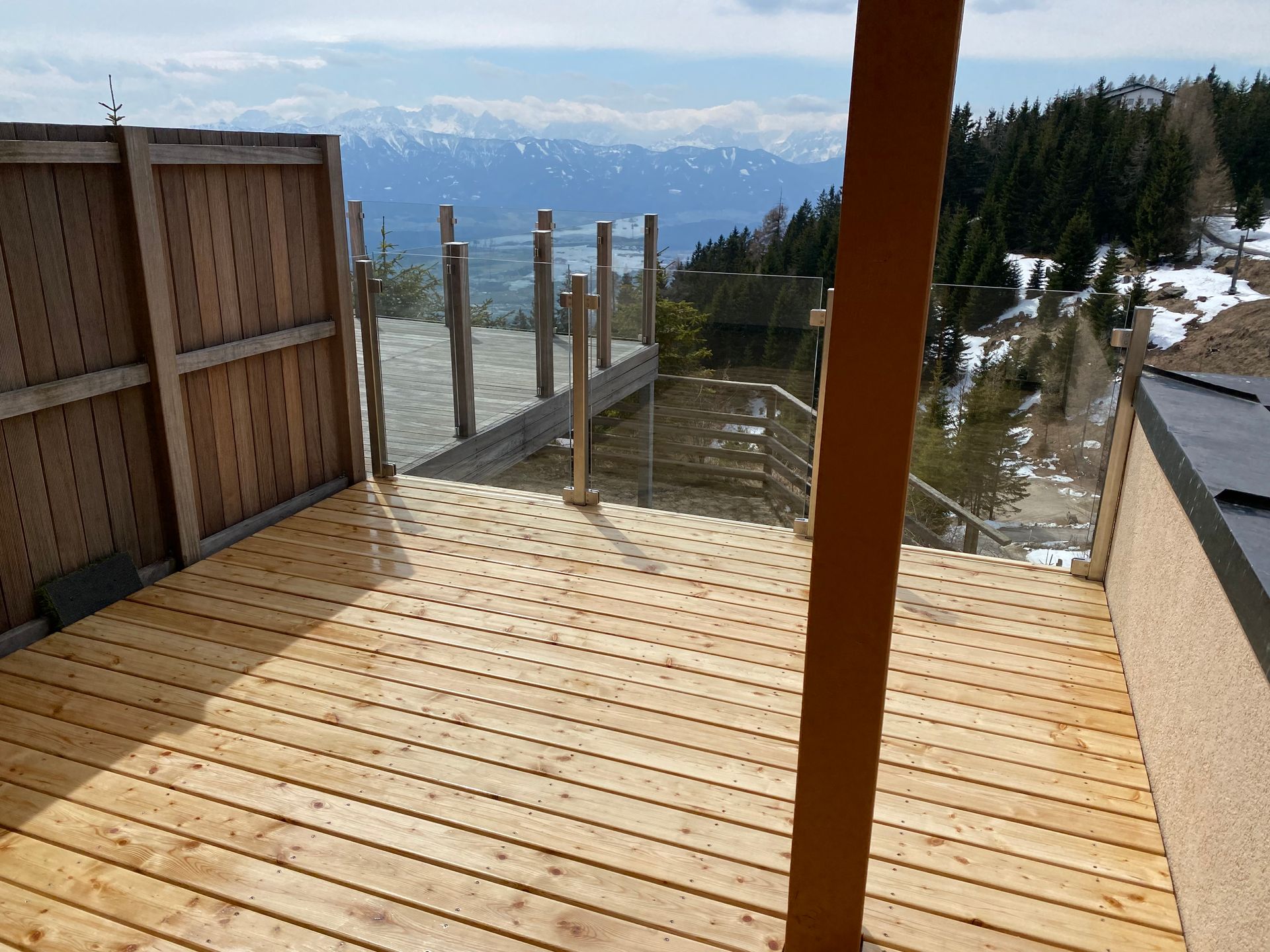 Holzterrasse mit Blick auf einen verschneiten See und die Berge in der Ferne