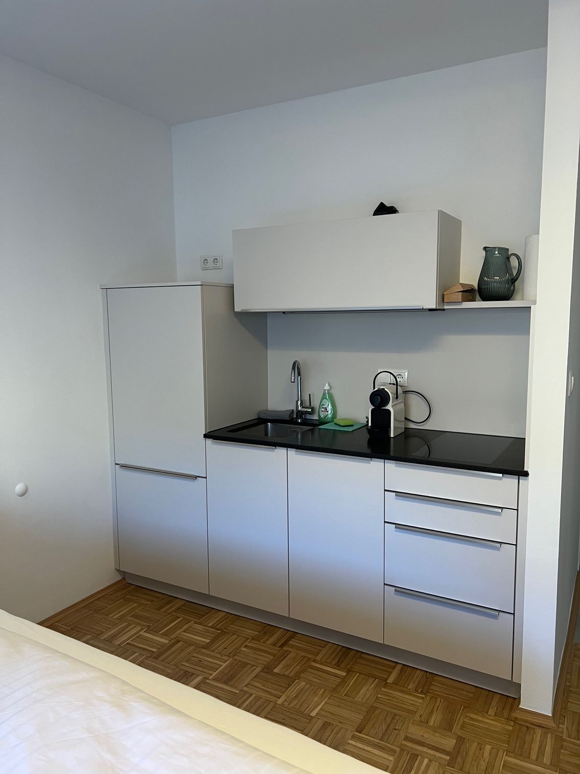 Kompakte weiße Küche mit Schränken, schwarzer Arbeitsplatte, Spüle und Parkettboden
