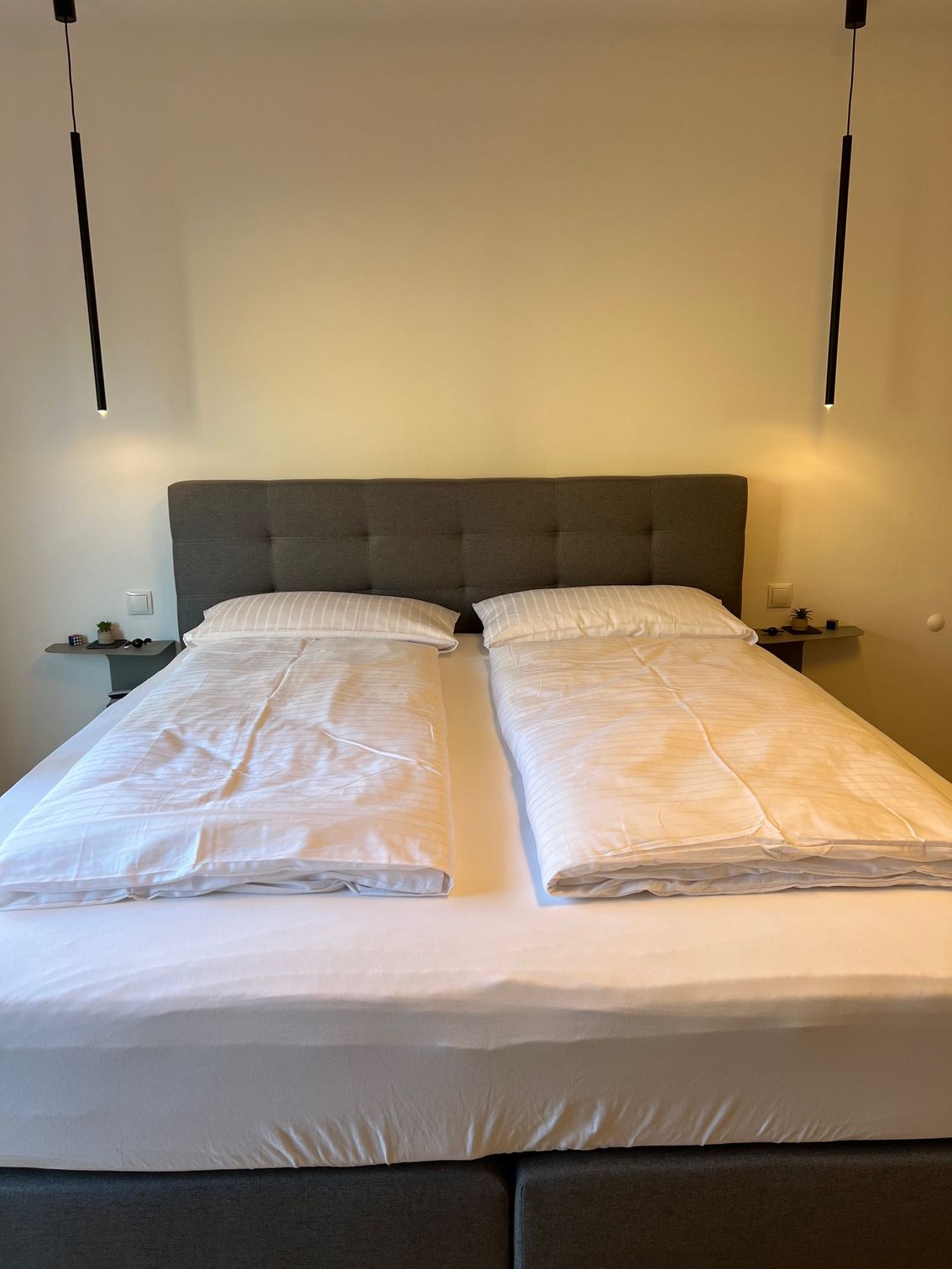 Ein ordentlich gemachtes Bett mit weißer Bettwäsche, zwei Kissen und einem grauen Kopfteil in einem Schlafzimmer