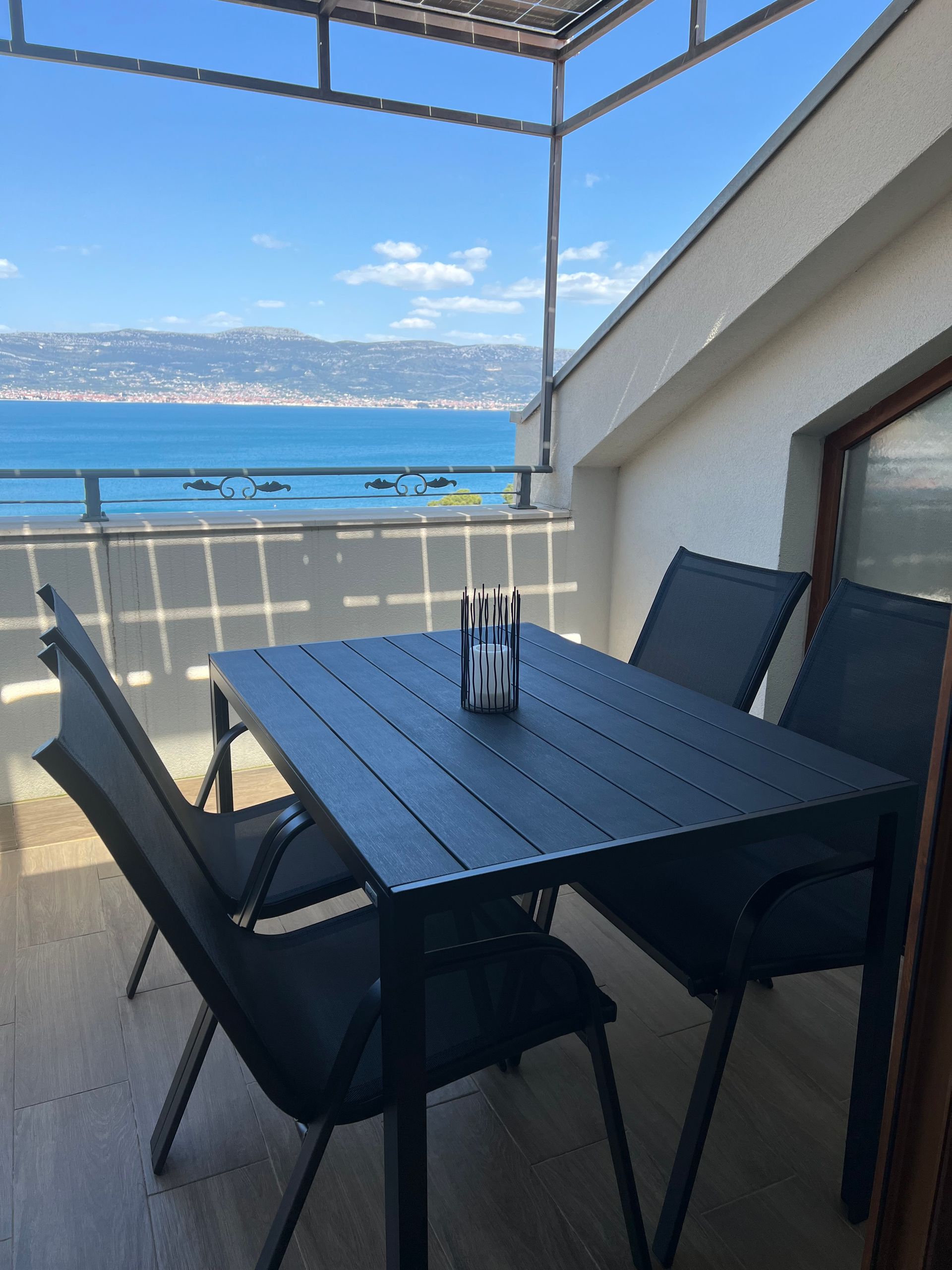 Balkon mit schwarzem Terrassentisch und Stühlen mit Blick auf einen blauen See und ferne Berge