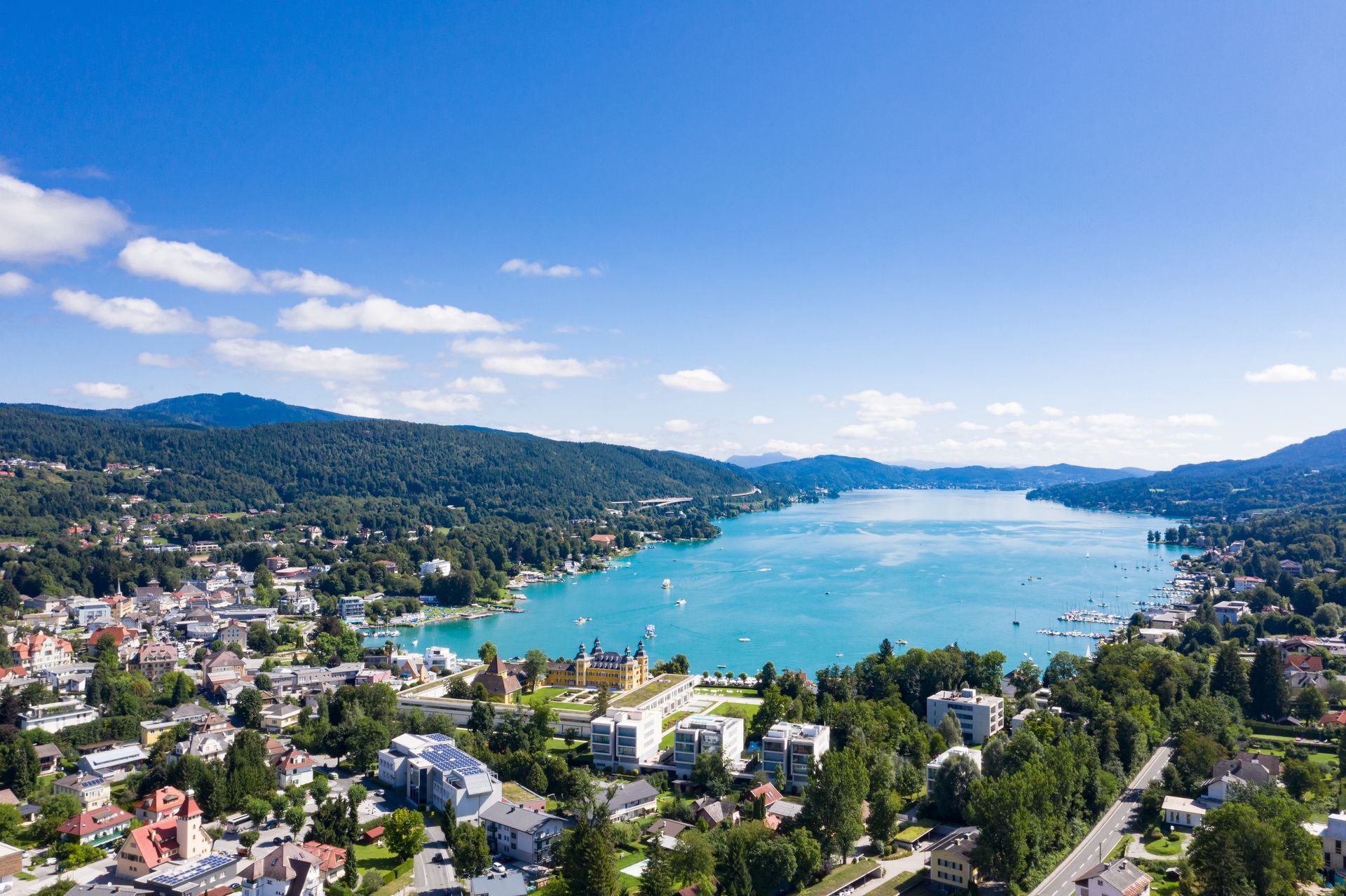 Panoramablick auf einen blauen See, umgeben von grünen Hügeln und einer Stadt unter klarem Himmel