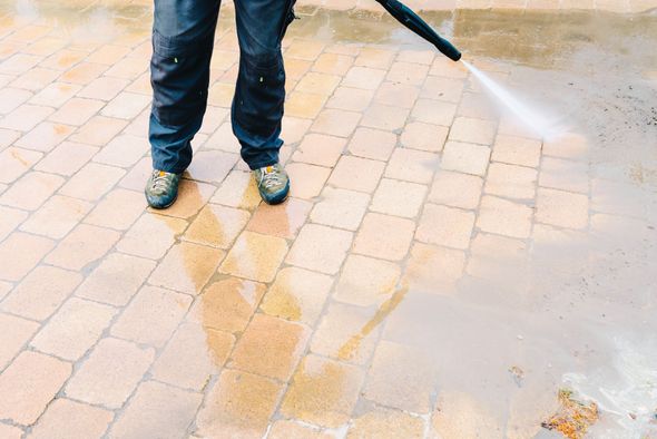 Person power washing a brick patio with water.
