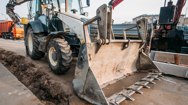 Backhoe loader with raised bucket on a construction site, beside other heavy machinery and workers
