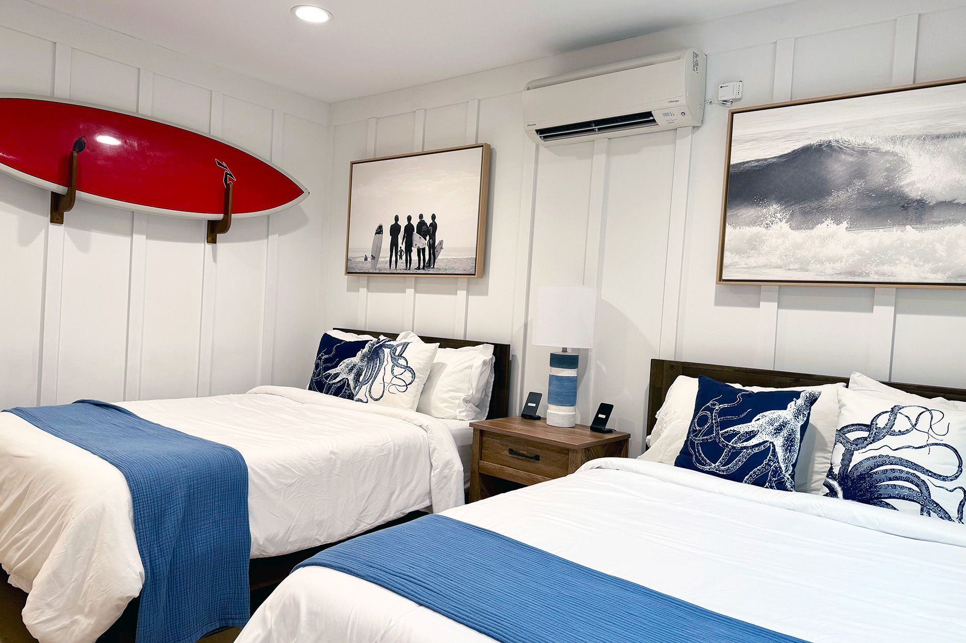 Surf Casita second bedroom with two full beds, blue bedding, a red surfboard on the wall and mini-split A/C