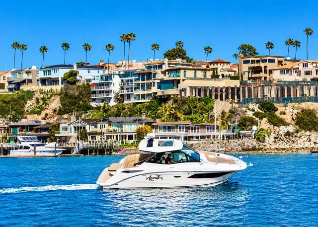 Boat cruising Newport Harbor past waterfront homes