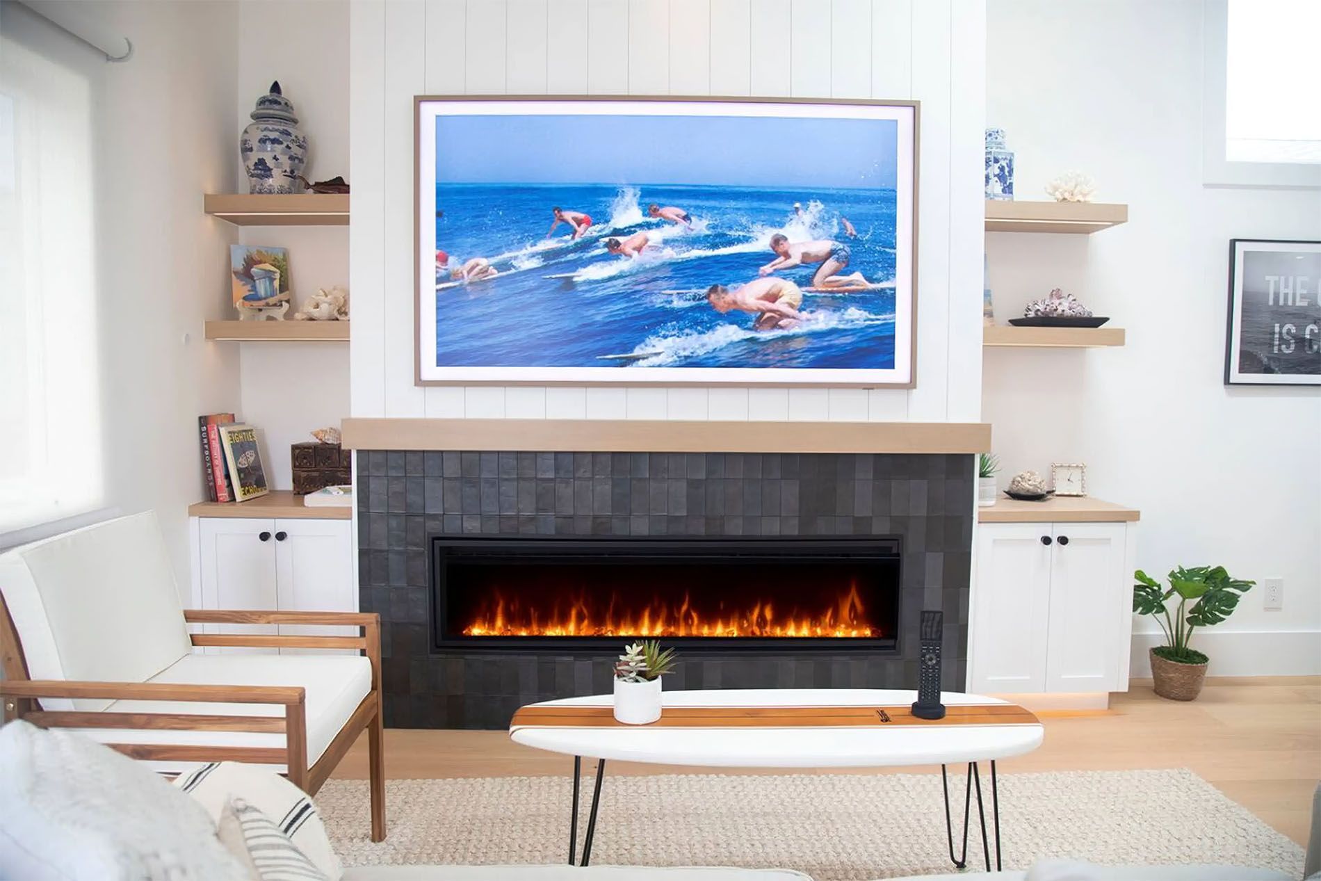 Modern living room with a lit fireplace, ocean painting, and white chairs and shelves