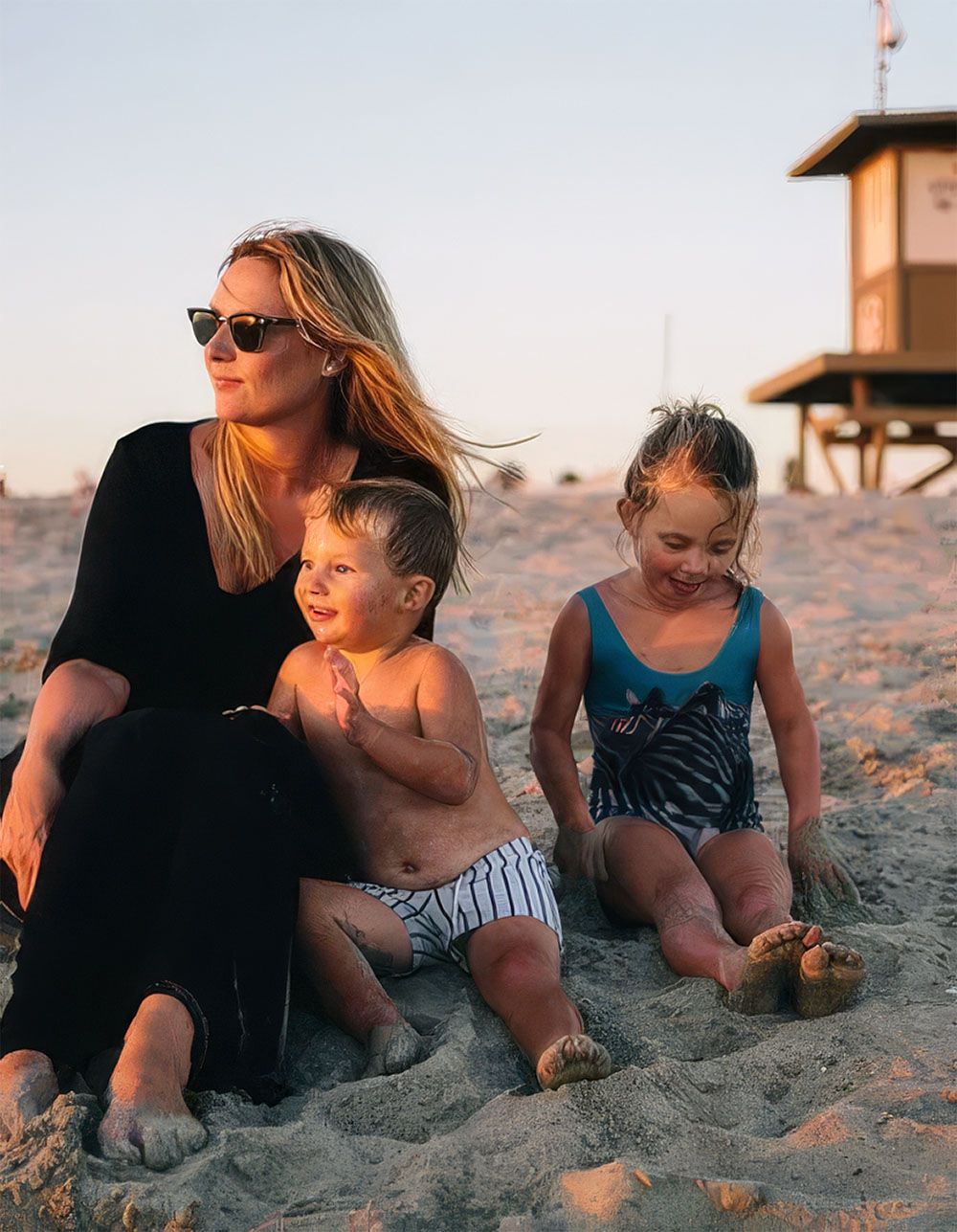 Mother and two young children relaxing on the sand by a Newport Beach lifeguard tower