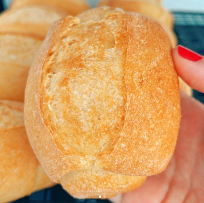 Uma pessoa com esmalte vermelho está segurando um pão na mão.