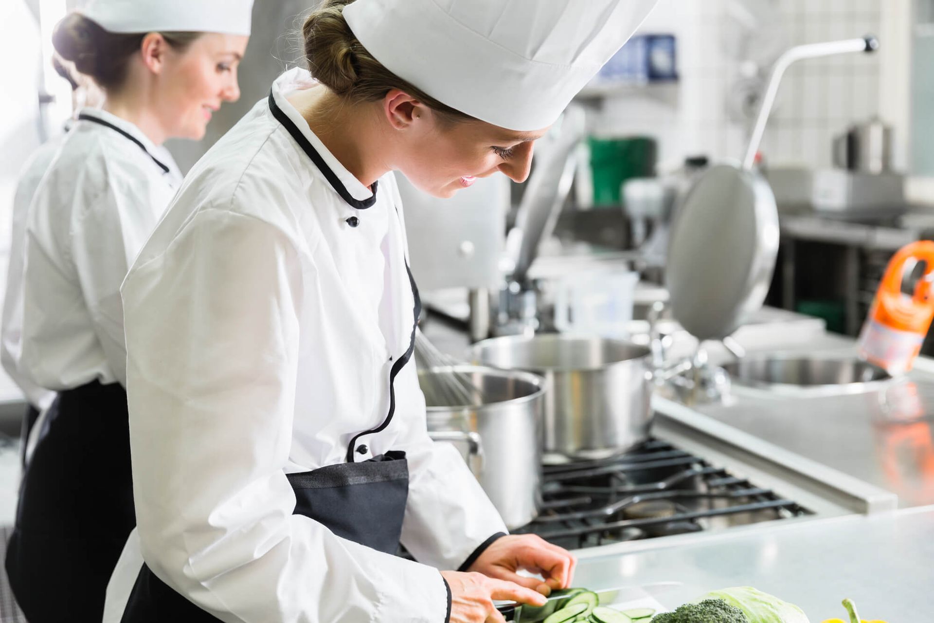 Duas chefs estão preparando comida em uma cozinha comercial.
