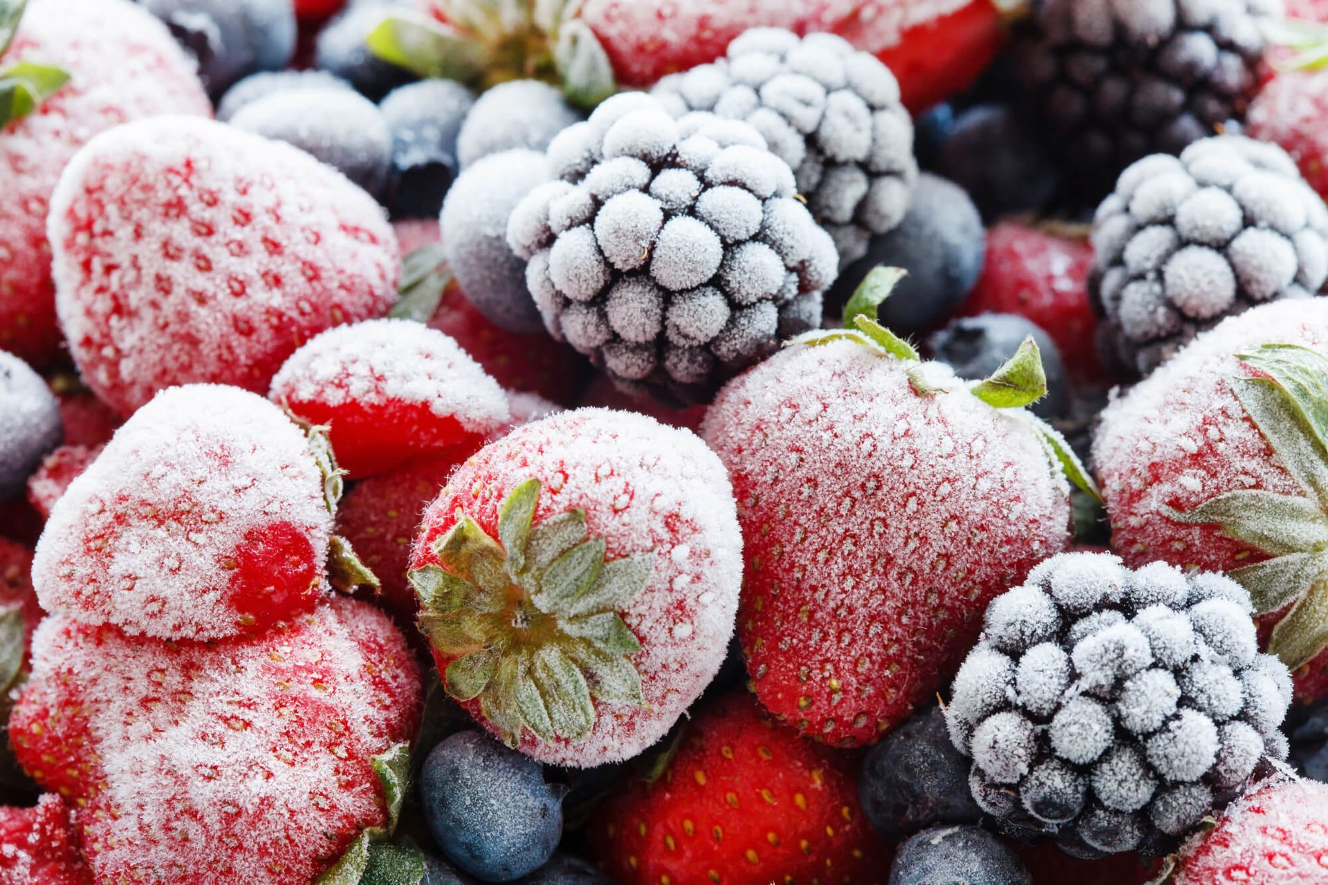 Uma pilha de frutas congeladas, incluindo morangos, mirtilos, framboesas e amoras cobertas de geada.