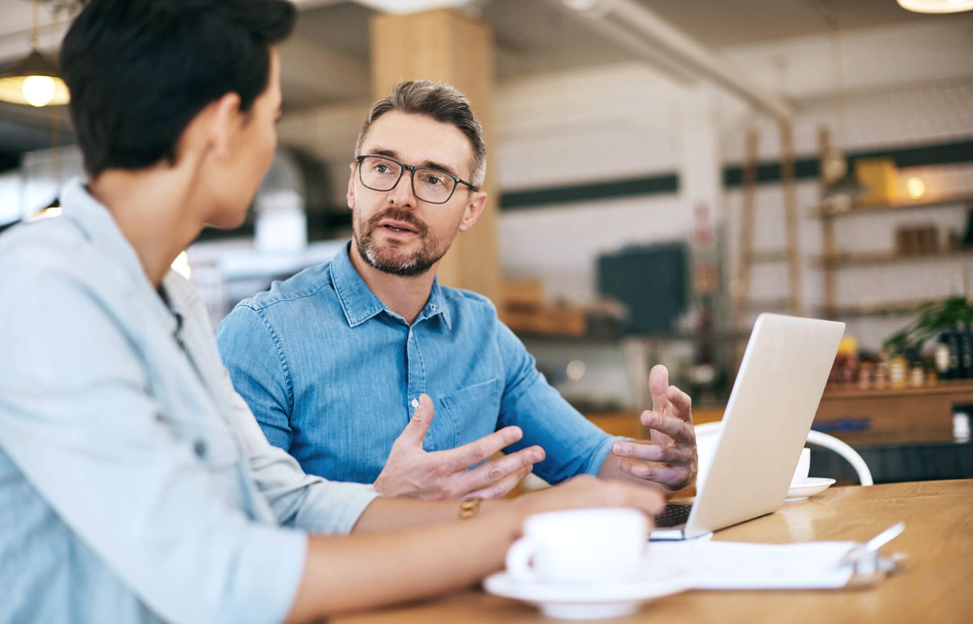 Um homem e uma mulher estão sentados à mesa conversando enquanto olham para um laptop.