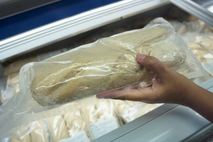Uma pessoa está segurando um saco de comida em frente a um freezer.