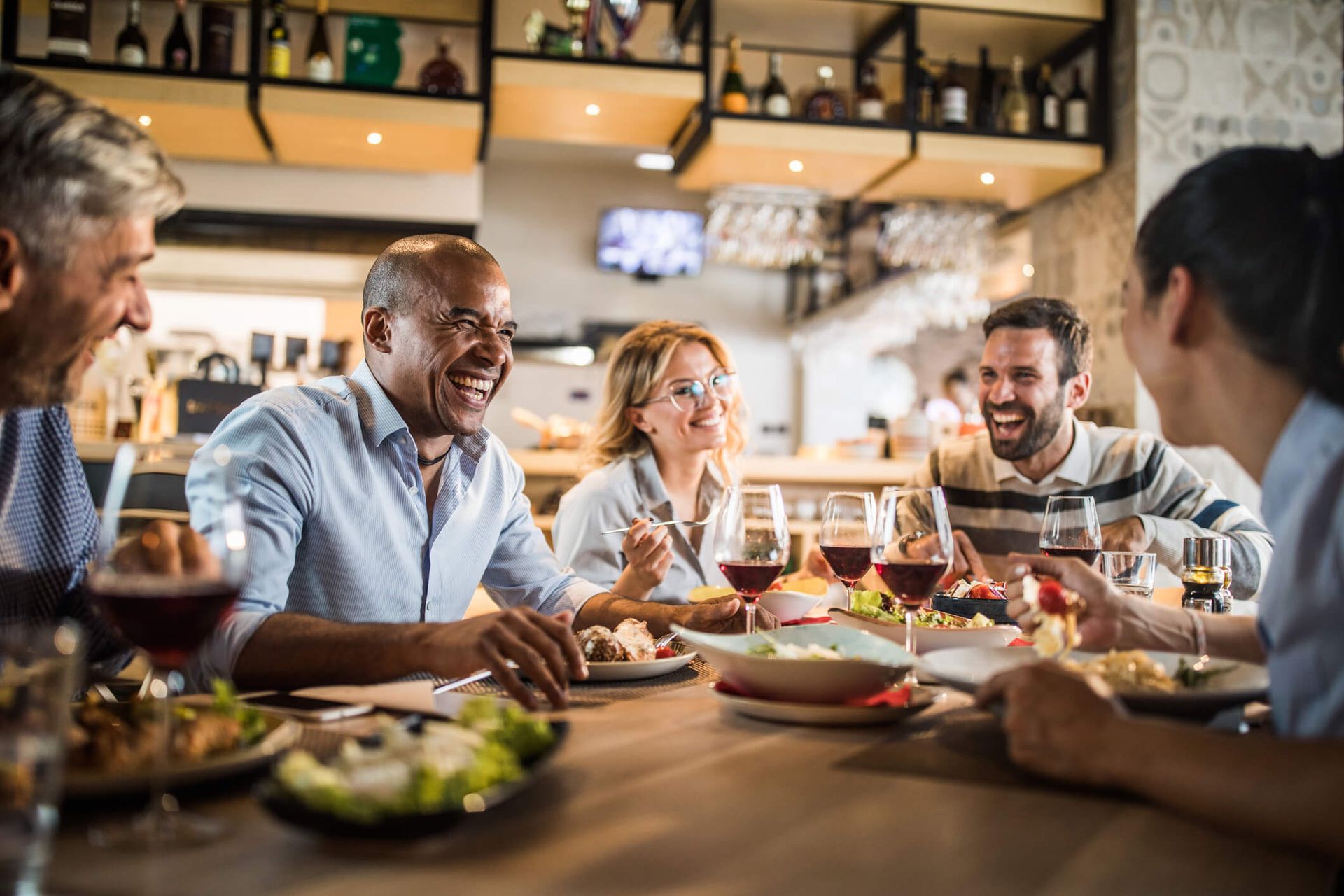 Um grupo de pessoas está sentado à mesa de um restaurante comendo e bebendo vinho.