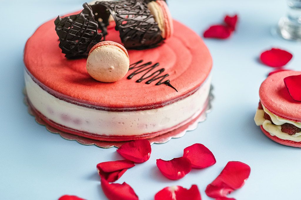 Um bolo vermelho e branco cercado por pétalas de rosas sobre uma mesa.