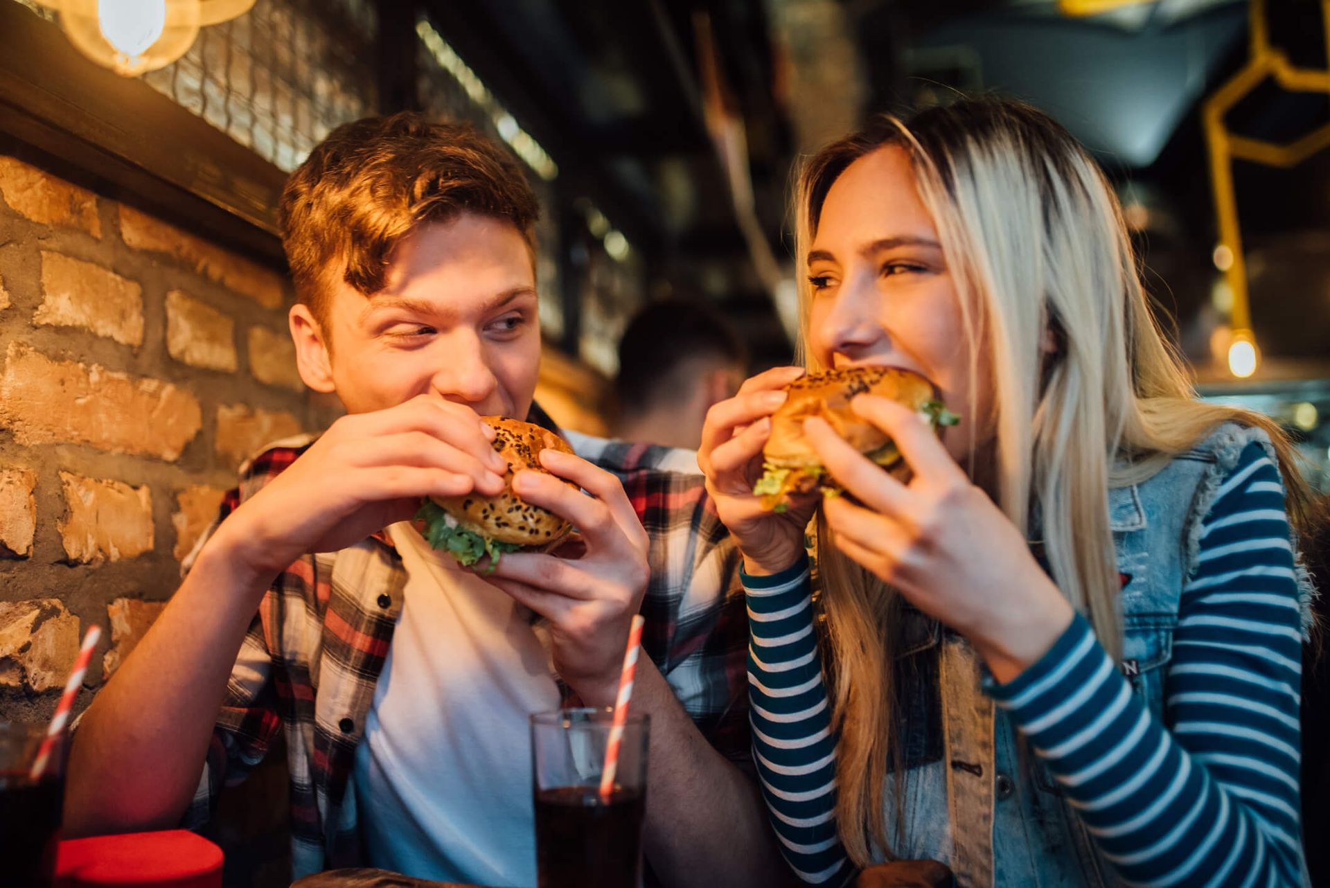 Um homem e uma mulher estão comendo hambúrgueres em um restaurante.