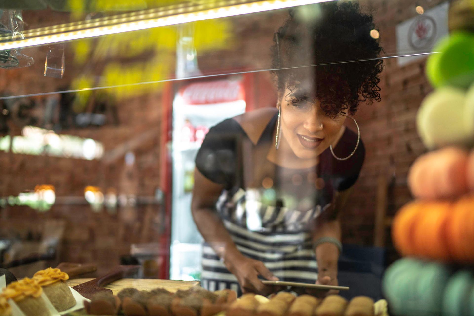 Uma mulher está parada atrás de uma vitrine de vidro em uma padaria.