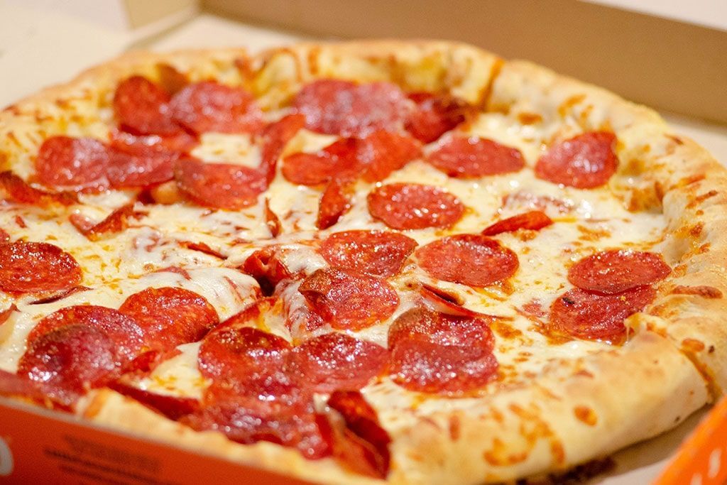 Uma pizza de calabresa está em uma caixa sobre uma mesa.