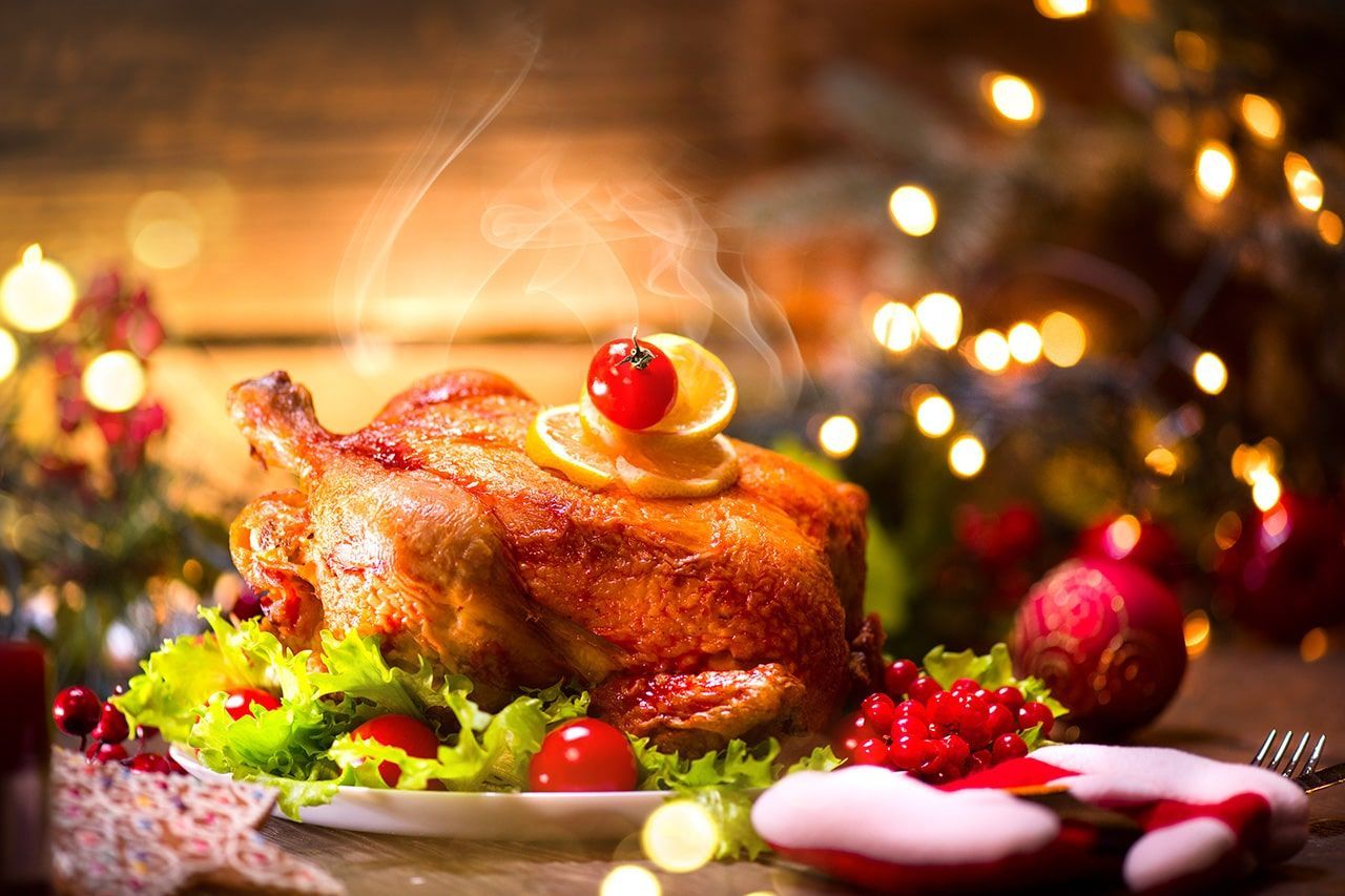 Um frango assado em um prato com legumes e uma árvore de natal ao fundo.
