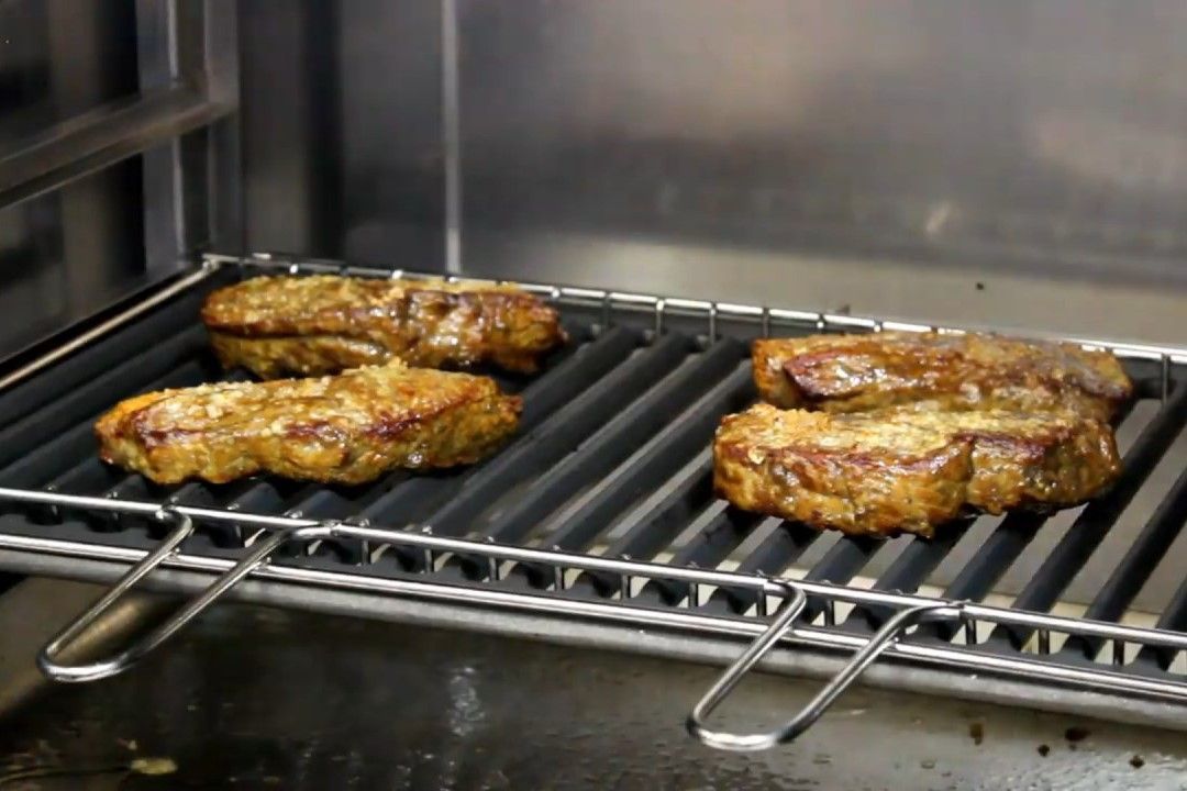 Três pedaços de carne estão cozinhando na grelha
