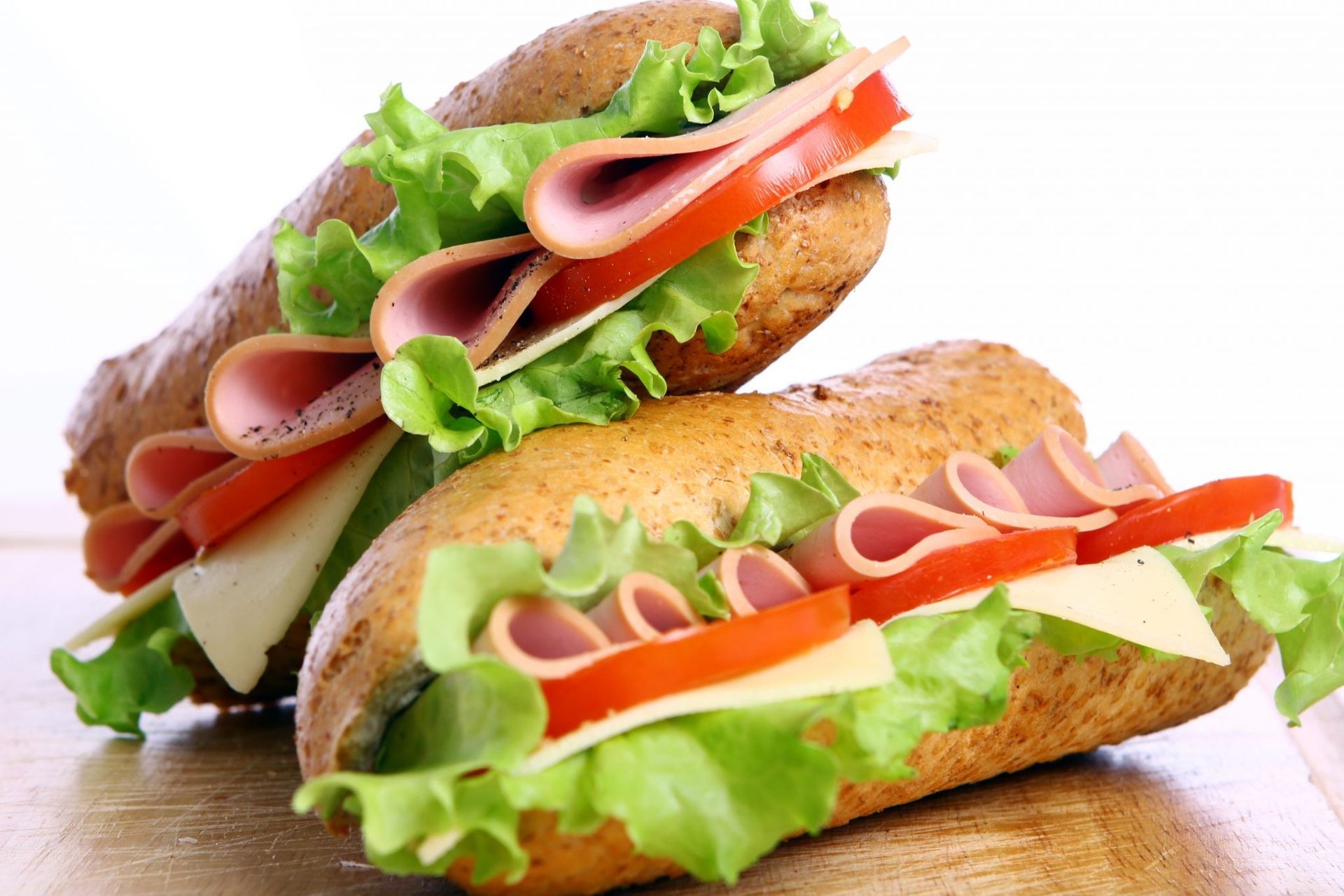 Dois sanduíches sub com presunto, alface e tomate em uma mesa de madeira