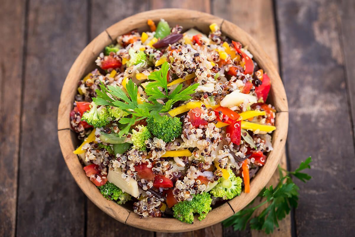 Uma tigela de madeira cheia de arroz e vegetais sobre uma mesa de madeira.