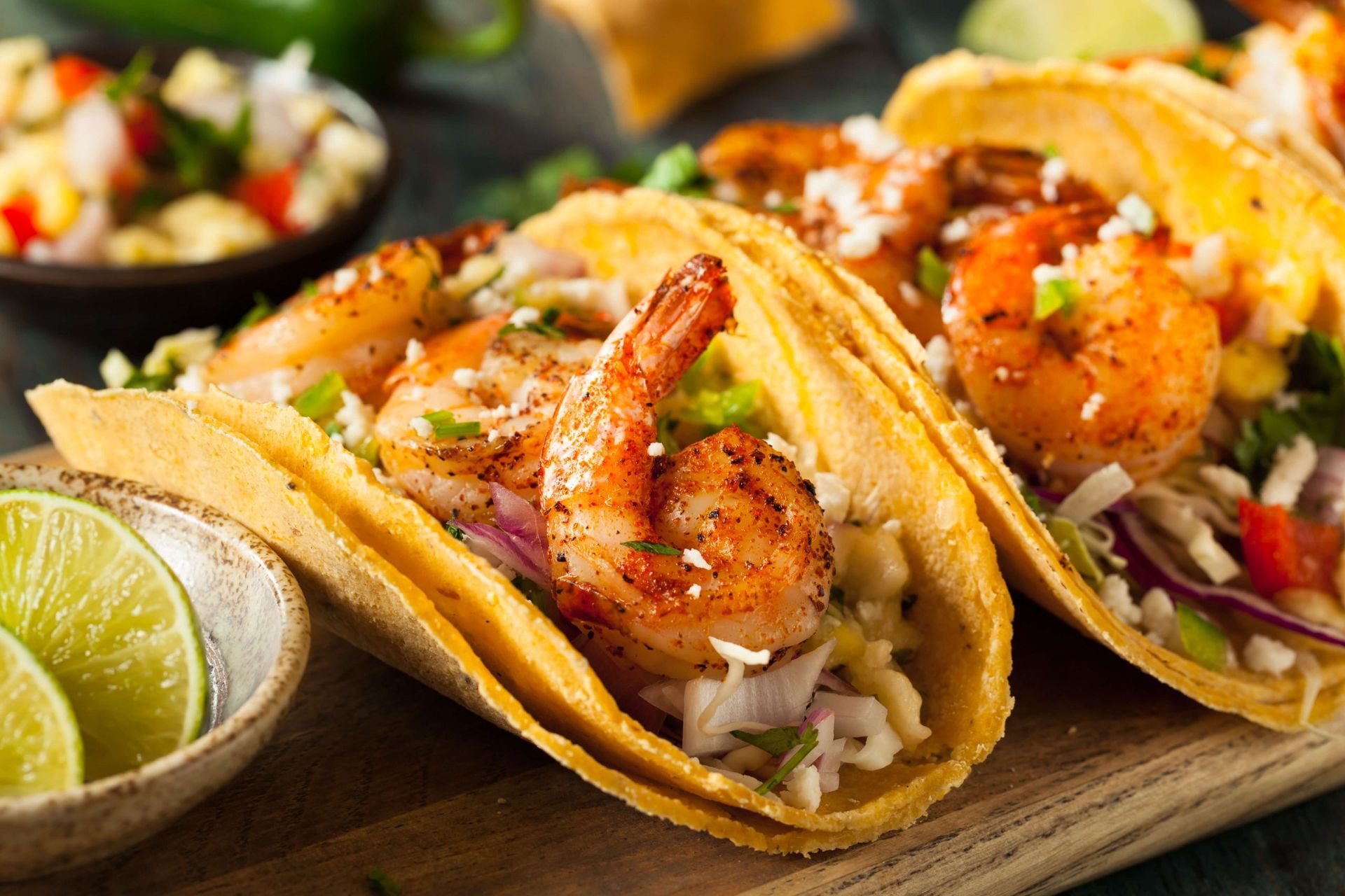 Um close de três tacos de camarão em uma tábua de corte de madeira.
